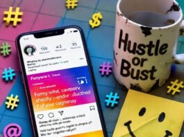 How to Promote Your Brand on Social Media Without Paid Ads Messy desk with chipped "Hustle or Bust" mug, phone, smiley note, colorful hashtags.